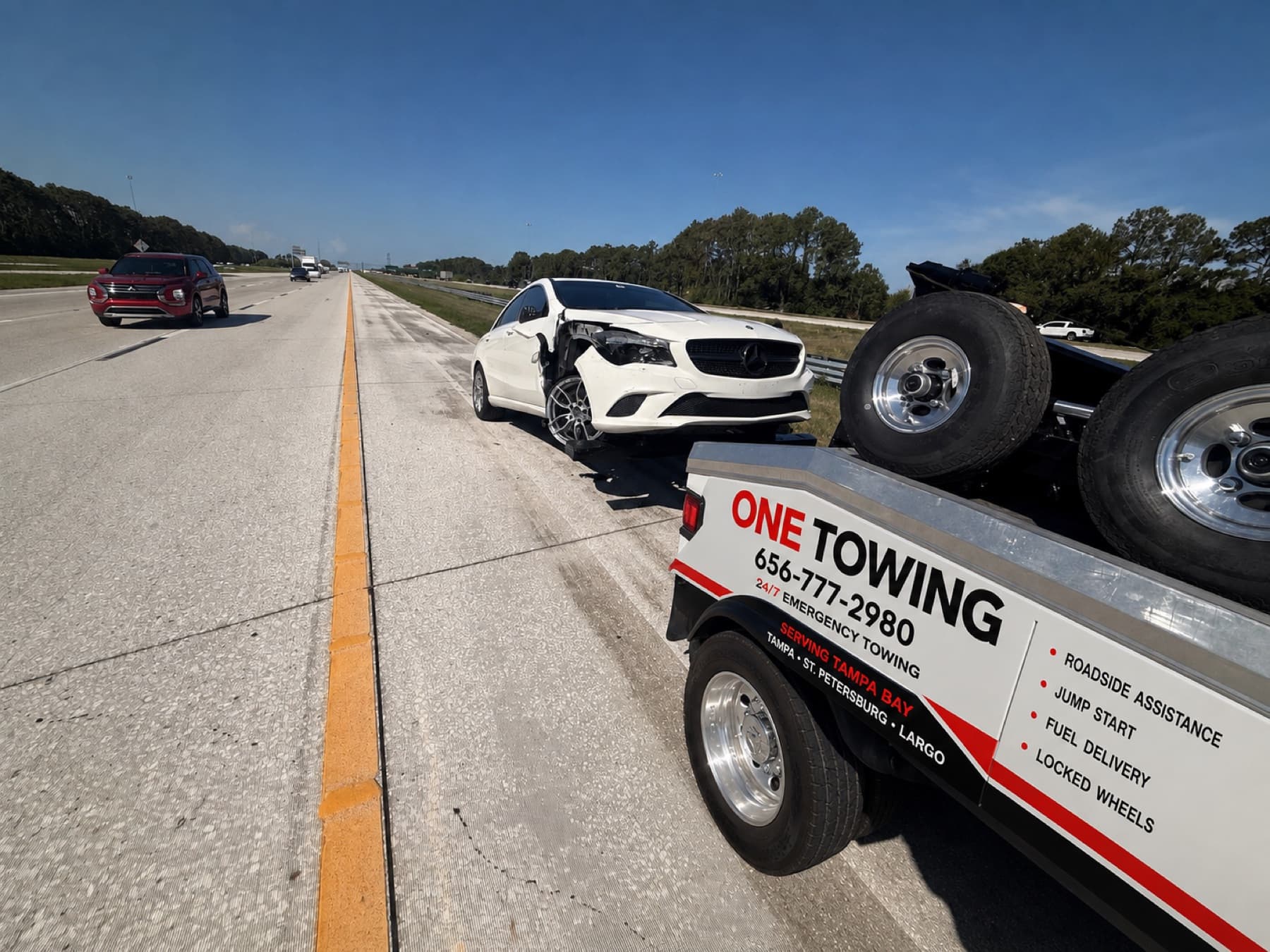 ONE TOWING wrecker loading a crashed Mercedes CLA on a Tampa Bay highway shoulder