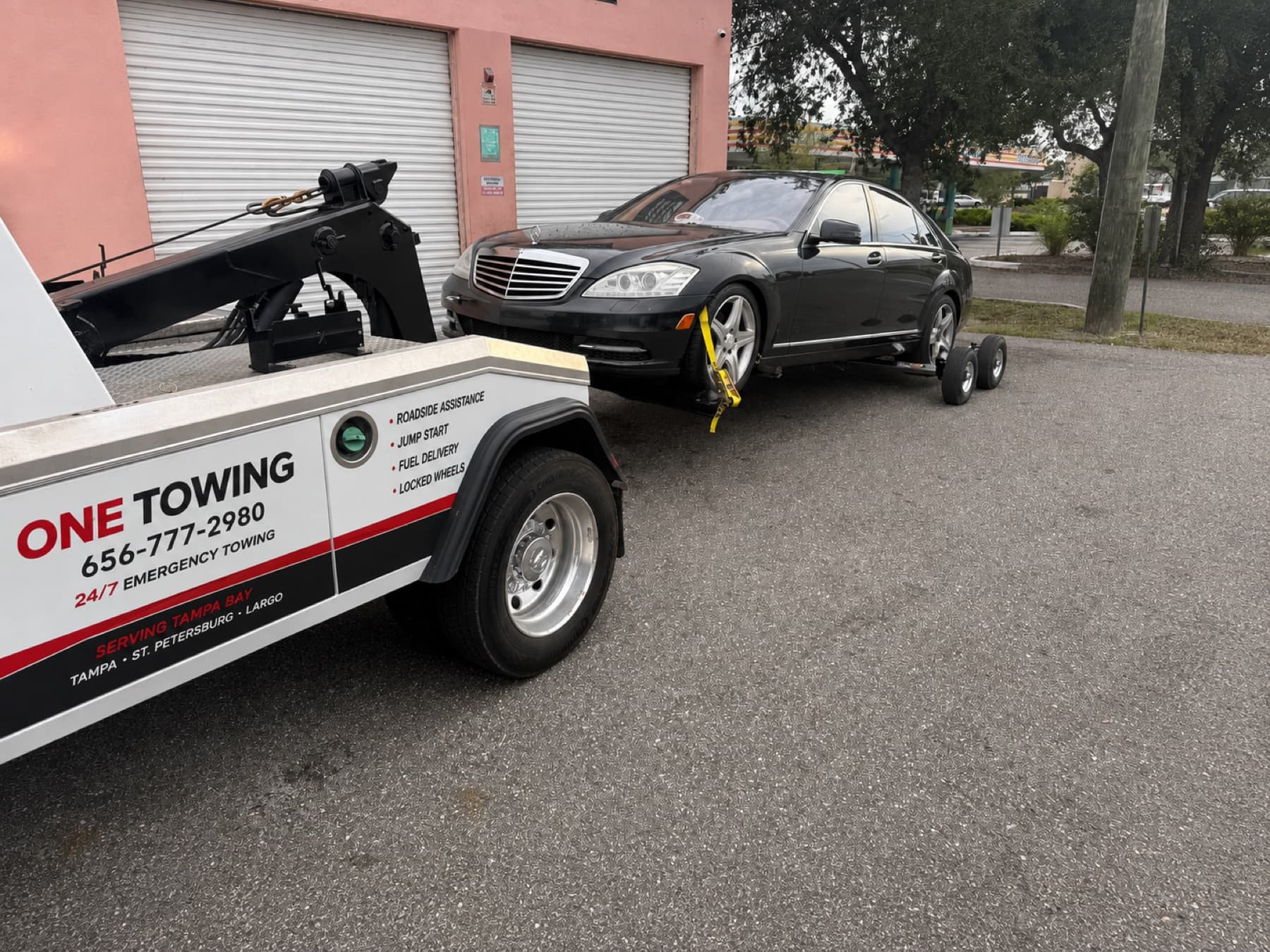 Mercedes-Benz S-Class loaded on dollies behind a ONE TOWING wrecker at a Tampa shop